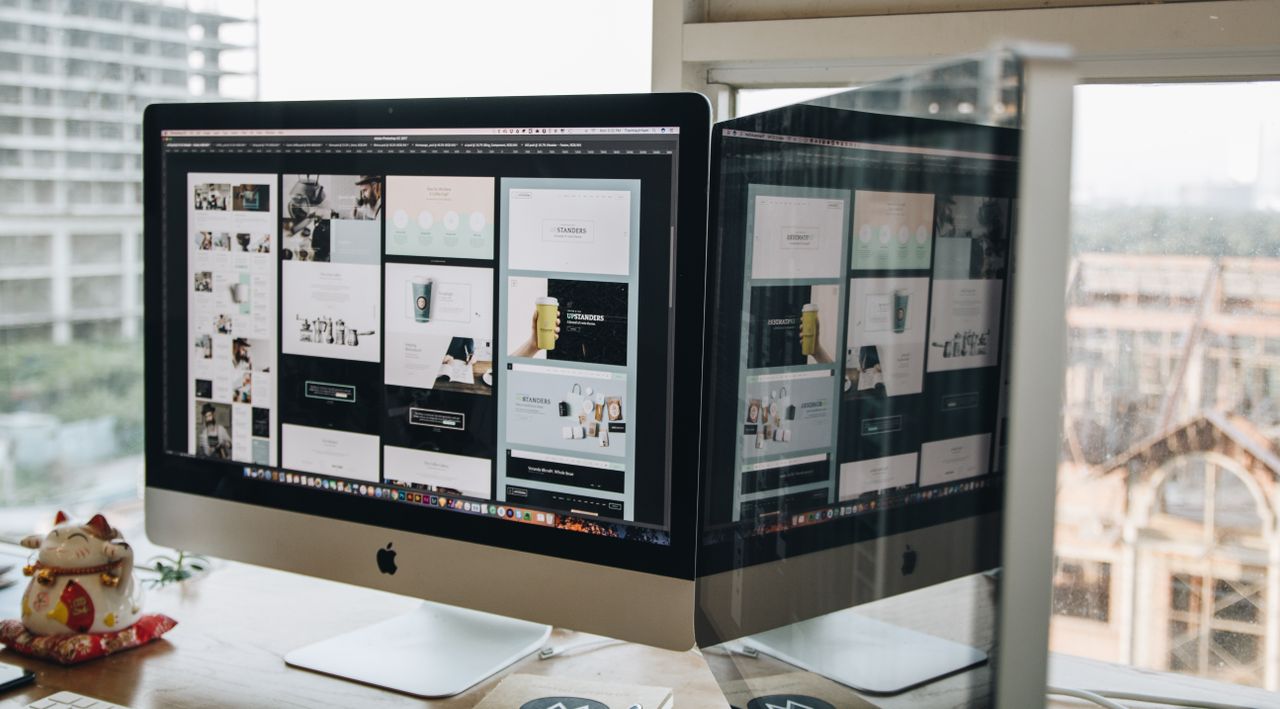 Two monitors on a desk, presenting web design in a sleek office environment.